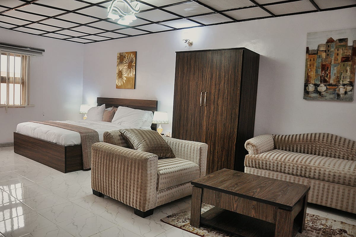 A modern bedroom with a bed, two armchairs, a sofa, a wooden cabinet, and artwork on the walls.