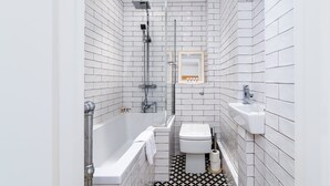 Ein Badezimmer mit weißen Fliesen, einer Badewanne, einer Toilette und einer Dusche.