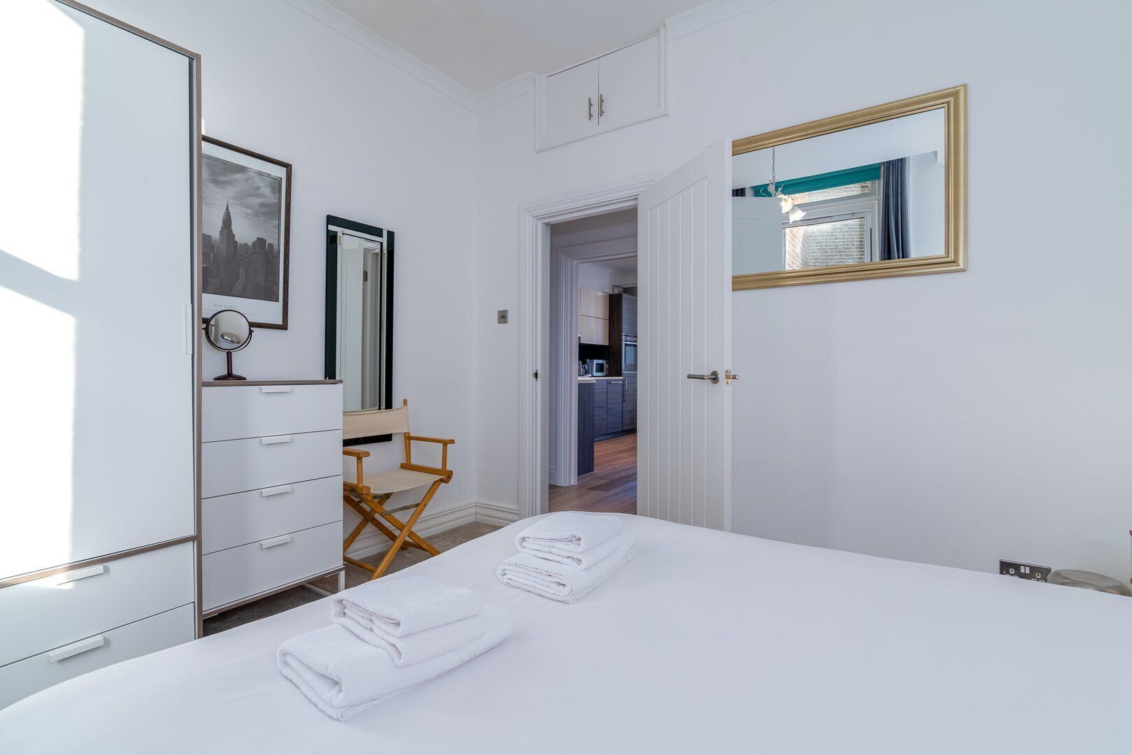 A hotel room with a bed, a desk, a chair, a wardrobe, a mirror, and a door leading to a bathroom.