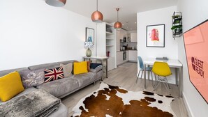 A modern living room with a grey sofa, a cowhide rug, and a dining area with yellow chairs. - GuestReady - Amazing spot near Gilbert Park (London)