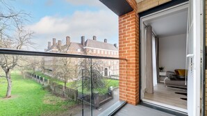A balcony with a glass door leading to a living room with a sofa and a plant. - GuestReady - Amazing spot near Gilbert Park (London)