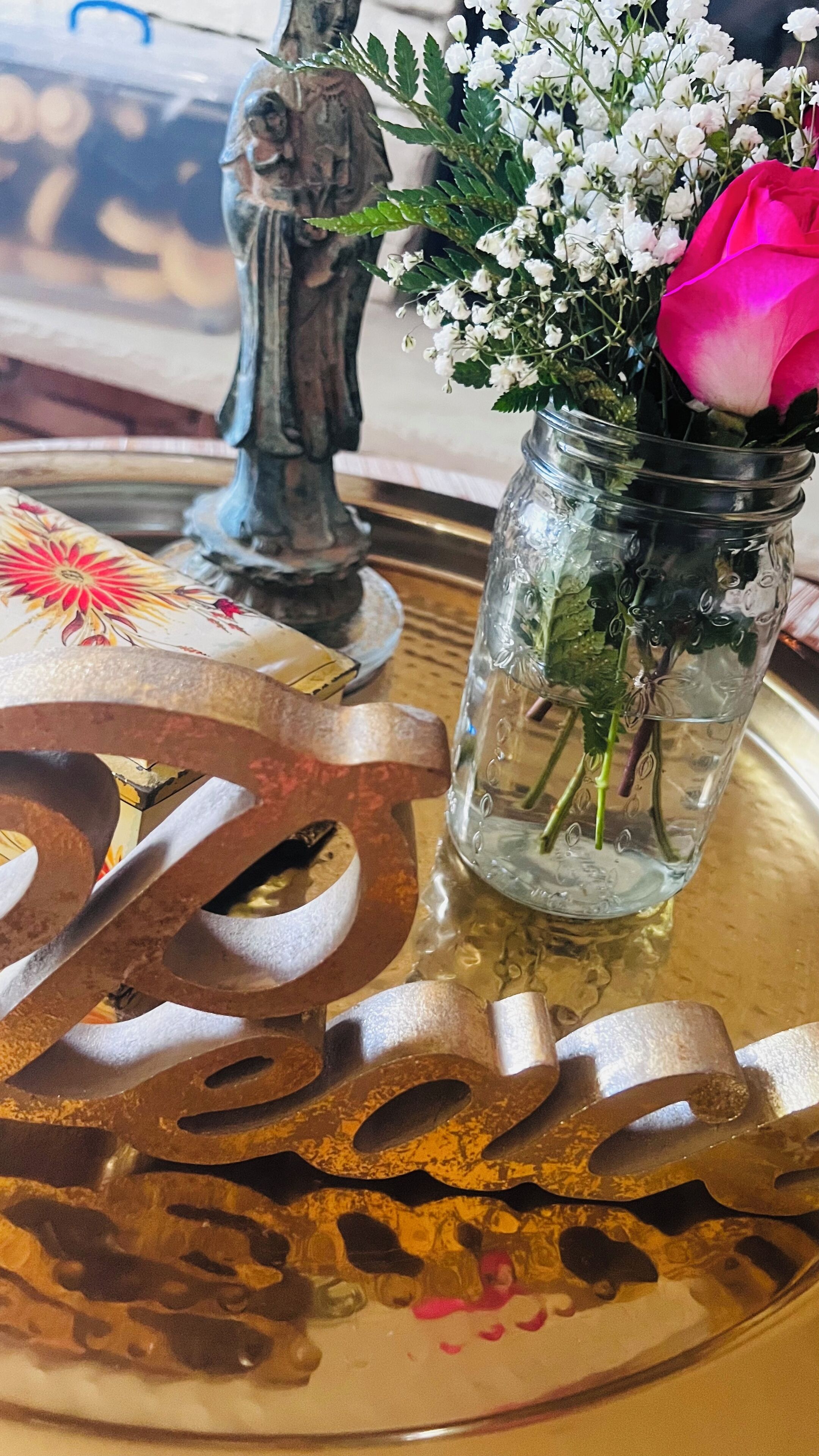 En metalkunstinstallation med tallet 20, et glas med blomster og en statue på et bord.