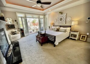 A spacious bedroom with a large bed, a ceiling fan, and a fireplace.