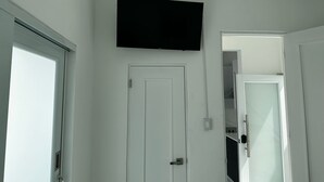 Een kamer met een witte deur, een flatscreen televisie erboven en een gedeeltelijk open deur naar een kast.