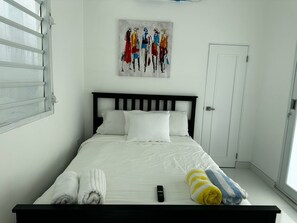 Een net opgemaakt bed met witte lakens, een afstandsbediening en handdoeken op het bed.