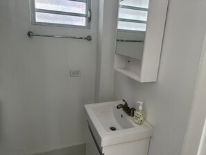 Een badkamer met een witte wastafel, een spiegel erboven en een raam met zonwering.