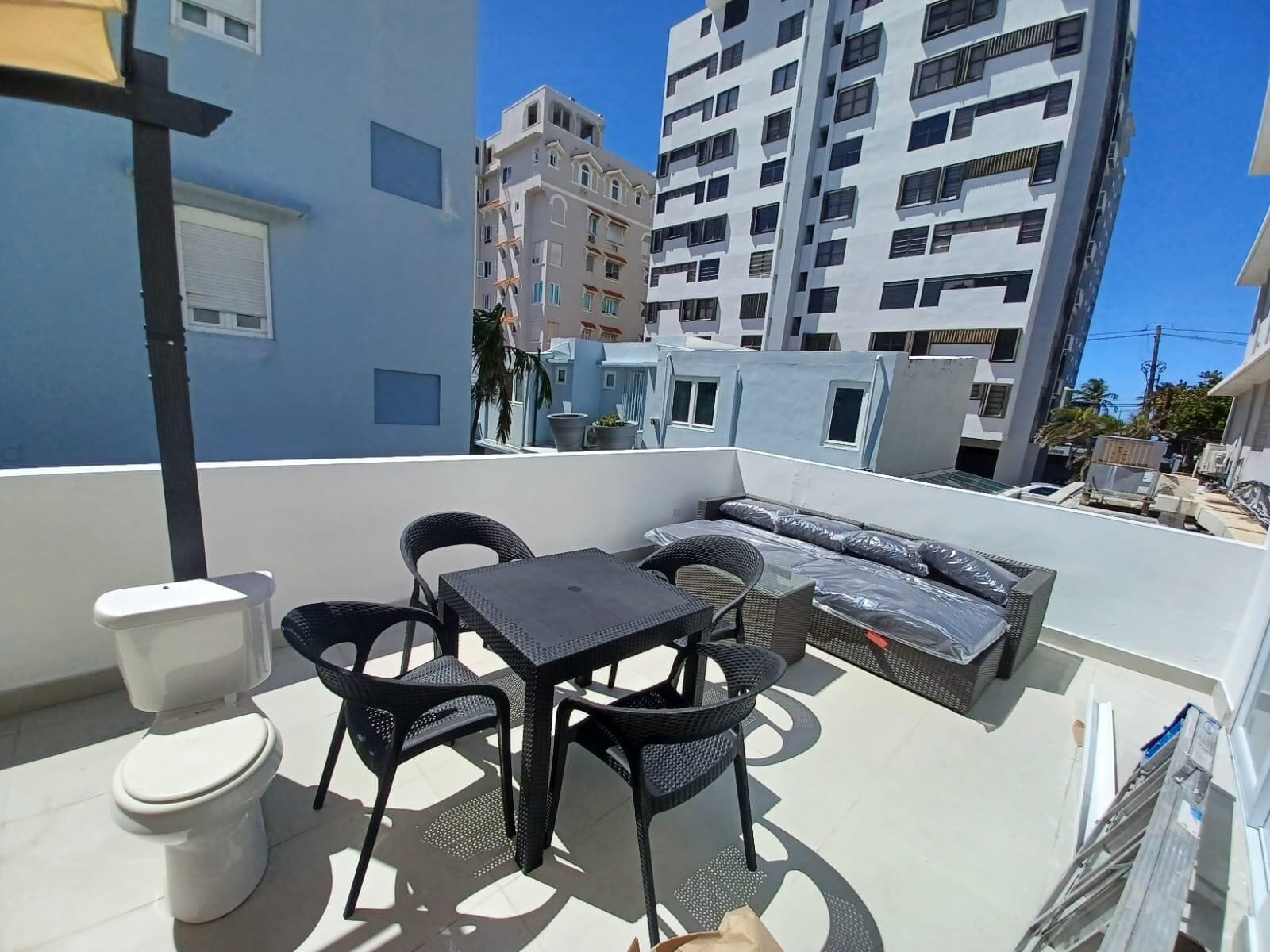 A rooftop terrace with a table, chairs, a sofa, and a toilet.