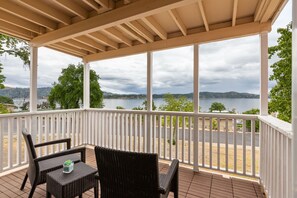 Relax in this serene outdoor space with a view of the water and distant hills, featuring a pair of wicker chairs and a small table.
