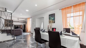 A modern dining area with a marble floor, black chairs, a white table, and orange curtains. - 3 bedroom lovely home in Jurdani (Jurdani)
