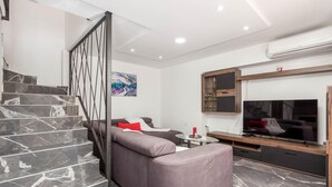 A modern living room with a marble staircase, a grey sofa, a flat-screen TV, and a glass coffee table. - 3 bedroom lovely home in Jurdani (Jurdani)
