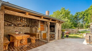 An outdoor patio with a stone wall, wooden furniture, and a brick floor. - 3 bedroom lovely home in Jurdani (Jurdani)