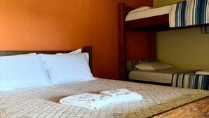 Una habitación con una cama litera de madera, una cama individual con ropa de cama blanca y un equipo de aire acondicionado en la pared.