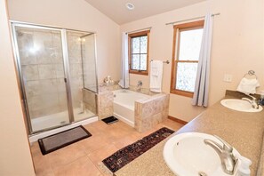 A bathroom with a glass shower enclosure, a bathtub, a sink, and a window with curtains.