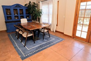 A dining area with a wooden table and chairs, a blue rug, a blue cabinet with glass doors, and a large plant.