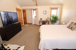 A bedroom with a bed, a TV on a dresser, a desk with a chair, and a window with curtains.