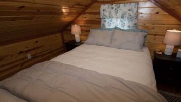 A cozy bedroom with a wooden ceiling, a bed with a beige duvet, two bedside tables with lamps, and a floral curtain.