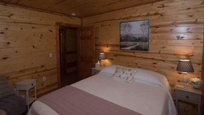 Ein Schlafzimmer einer Holzhütte mit einem Bett, Nachttischlampen und einem Bild an der Wand.