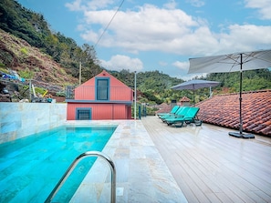 Una piscina con un edificio rojo al fondo, rodeada de abundante vegetación.