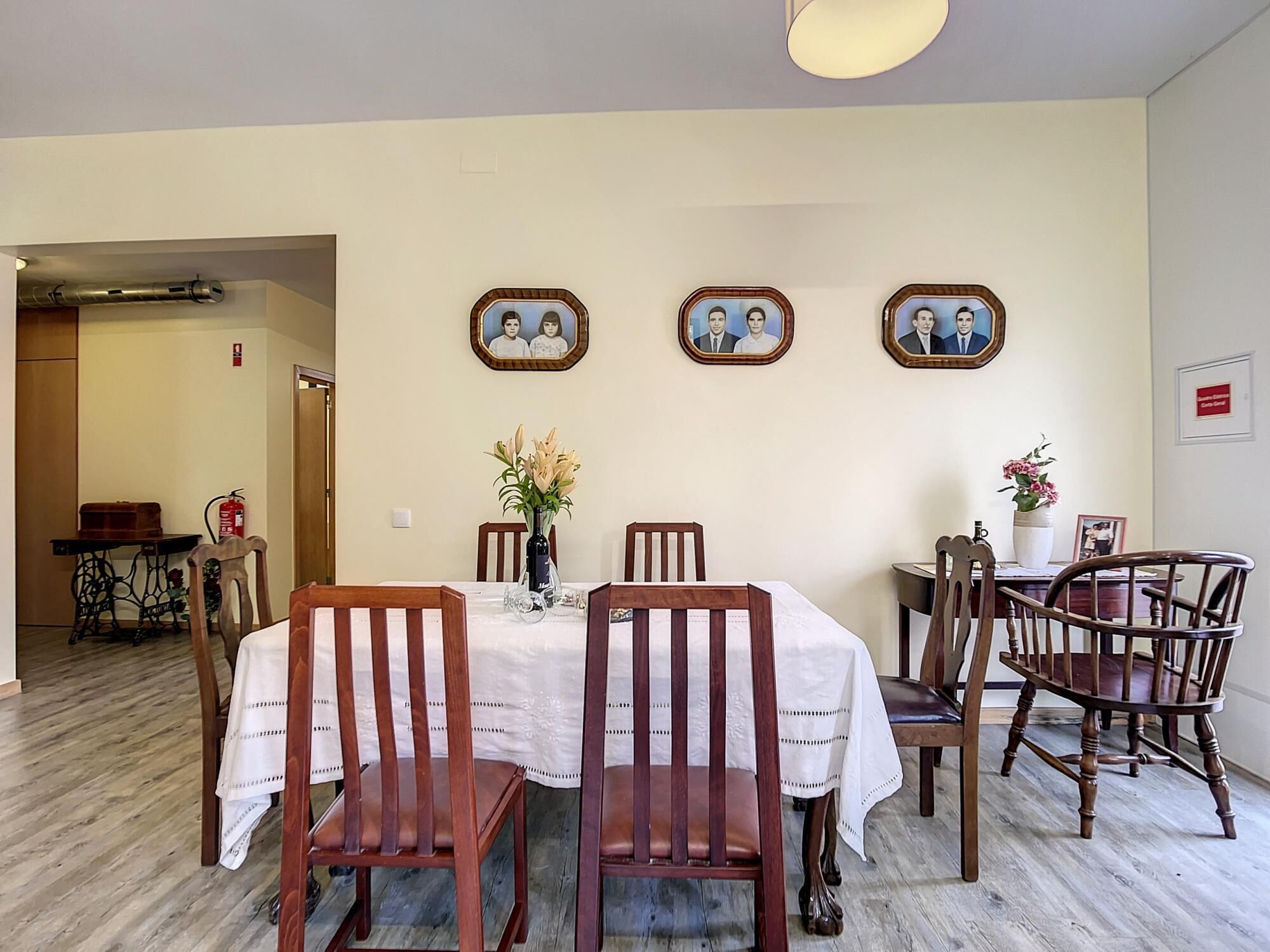 A dining area with a table set for four, surrounded by wooden chairs. There are framed pictures on the wall above the table.