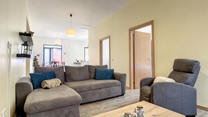 A modern living room with a grey sectional sofa, a wooden coffee table, and a grey armchair. - Avo Maria House by Atlantic Holiday (São Vicente)