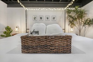 A neatly made bed with a wicker basket containing two towels and a tag.