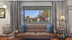 A living room with a brown sofa, patterned cushions, a side table with a lamp, and a chair. - ~CBS Featured~ HUGE HOT TUB|CINEMA|Firepit (South Bend)