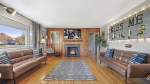 A modern living room with leather sofas, a fireplace, a TV, and a large wall decoration. - ~CBS Featured~ HUGE HOT TUB|CINEMA|Firepit (South Bend)
