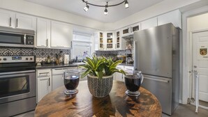 A modern kitchen with white cabinets, stainless steel appliances, and a wooden dining table with two glasses of red wine and a potted plant. - ~CBS Featured~ HUGE HOT TUB|CINEMA|Firepit (South Bend)