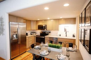 A modern kitchen with stainless steel appliances, wooden cabinets, and a dining area with a table set for four. - Luxe & Fully Stocked in Park City-Steps to Lift! (Park City)