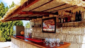 Eine Bar im Freien mit einer Steinwand, einem Strohdach und einem Plakat, das 'The Astari Bar' bewirbt.