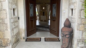 Ein Eingang mit Steinwänden, zwei Holztüren, einer Fußmatte und einer Buddha-Statue.
