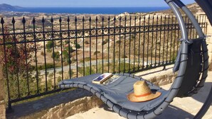 Ein Balkon mit Blick auf eine Küstenlandschaft, einem Metallzaun und einem Kissen mit Hut und Buch.