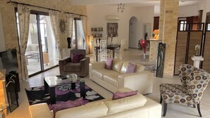 Ein geräumiges Wohnzimmer mit einem weißen Sofa, einem gemusterten Sessel und einem Glastisch.