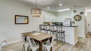 Una cocina moderna con armarios blancos, una mesa de comedor de madera y una lámpara colgante.