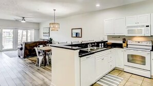 Una cocina moderna con gabinetes blancos, una isla central y una zona de comedor con sofá y sillas.