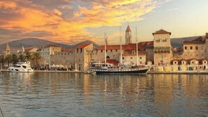 A waterfront scene with a historic building, a boat docked at the pier, and a clear sky. - Villa with pool 50 m from the sea (Okrug Gornji)