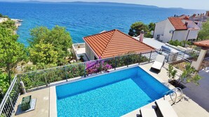 A swimming pool with a view of the sea, surrounded by greenery and buildings with red-tiled roofs. - Villa with pool 50 m from the sea (Okrug Gornji)