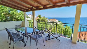 A covered outdoor patio with a table and chairs, a view of the sea, and a balcony railing. - Villa with pool 50 m from the sea (Okrug Gornji)
