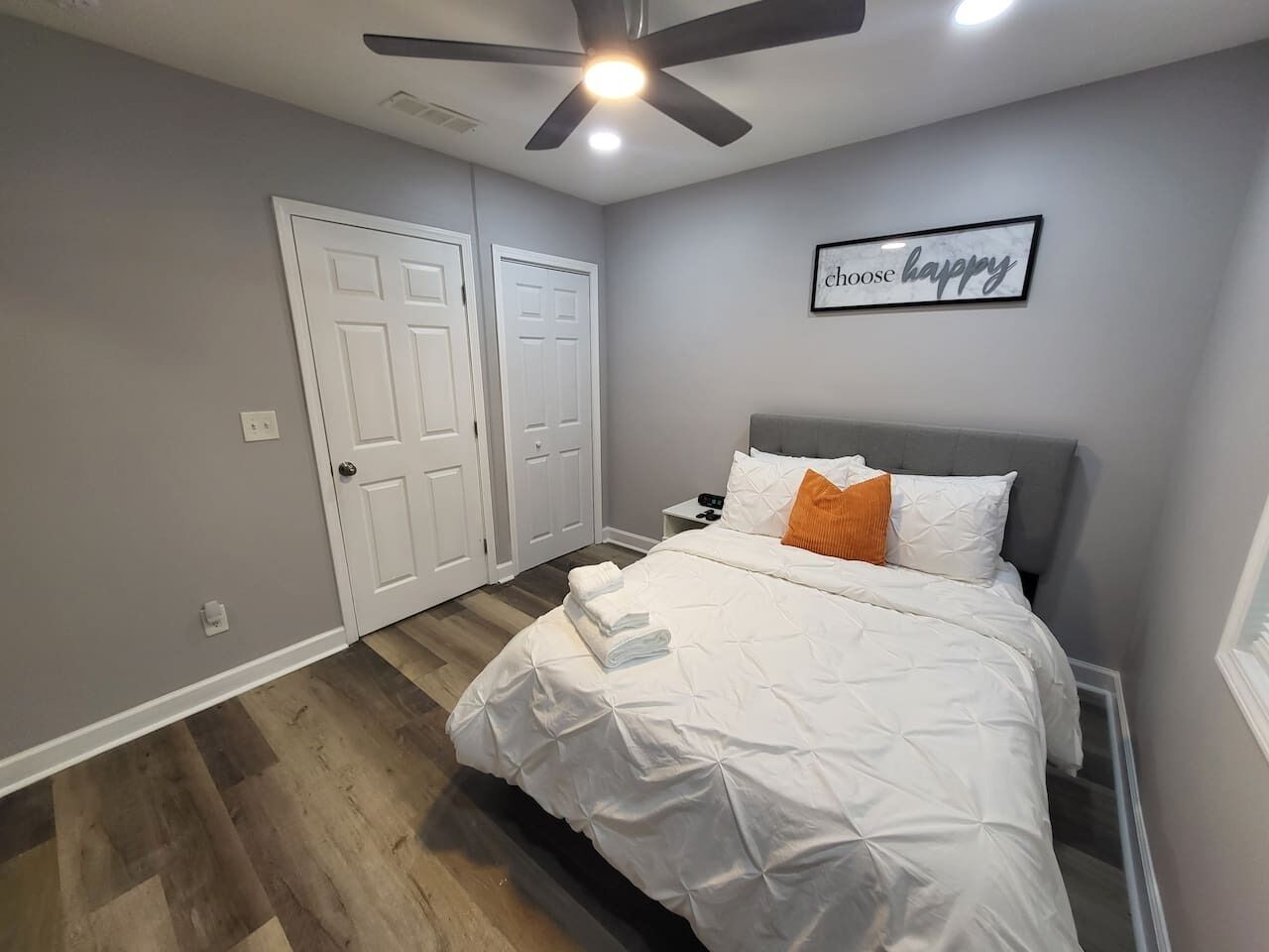 A bedroom with a bed, a ceiling fan, and a wall with a 'choose happy' sign.