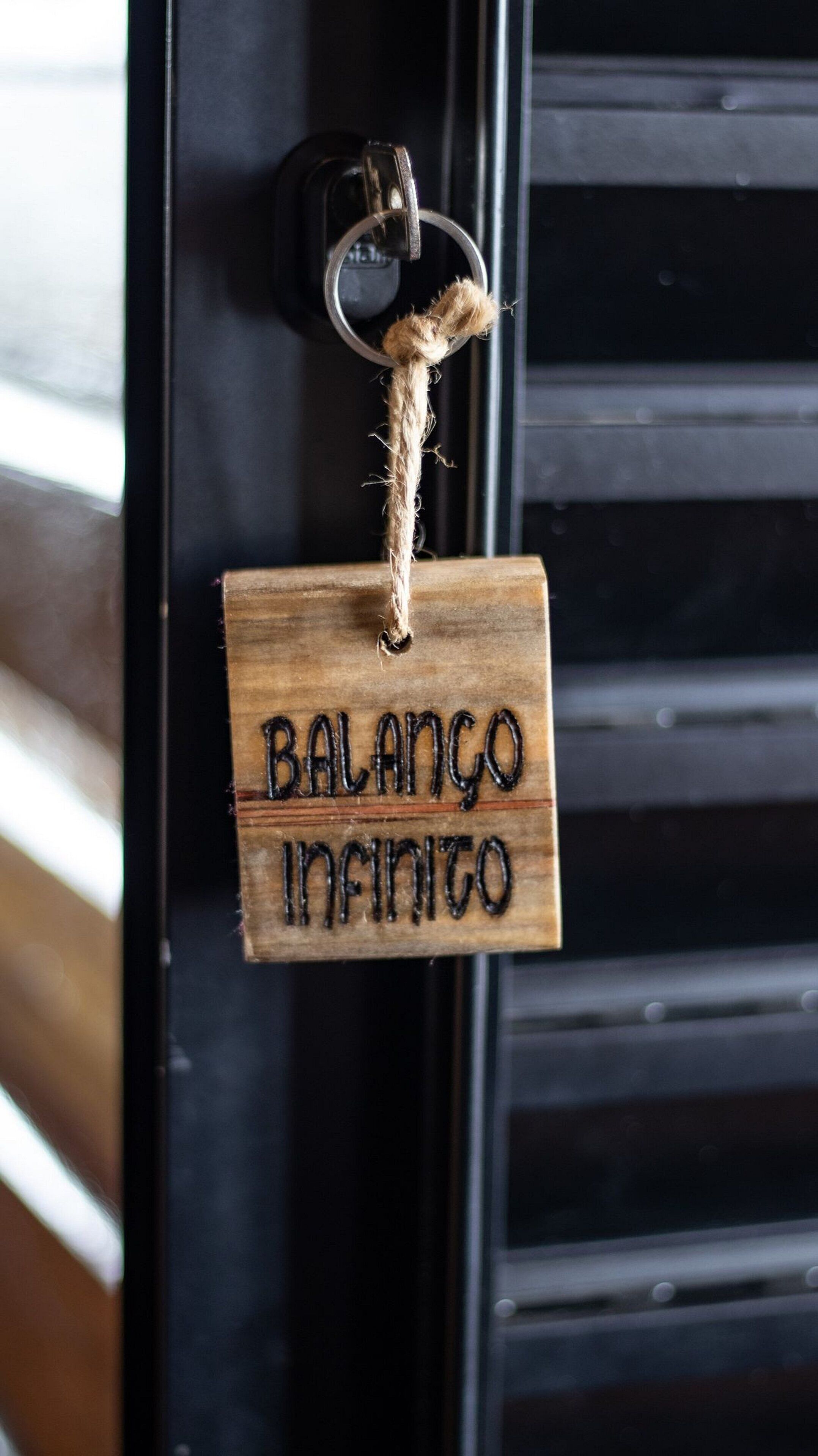 A wooden keychain with the text "BALANCO INFINITO" hanging on a black door.