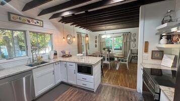 A modern kitchen with a wooden floor, white cabinetry, and a dining area with a table and chairs.