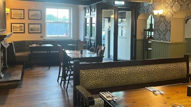 Un restaurante con piso de madera, una mesa de comedor central y una zona de estar con bancos.