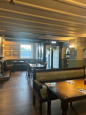 A restaurant interior with wooden tables and benches, a bar area, and framed pictures on the walls. - The Bayley Arms (Clitheroe)