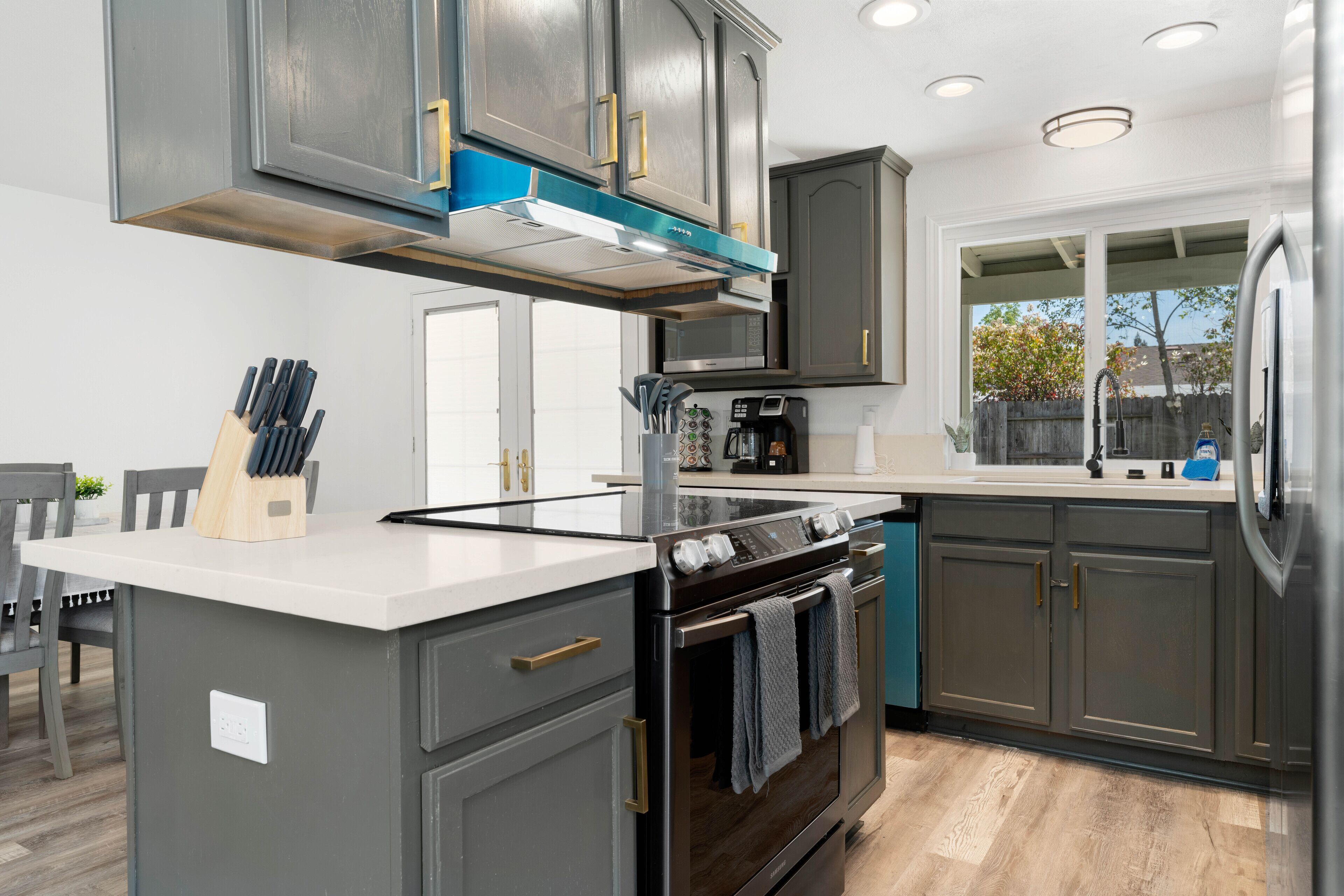 A modern kitchen with dark cabinets, a central island, and a built-in oven.