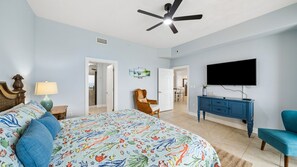 A bedroom with a bed, a ceiling fan, a TV, a dresser, and a chair.