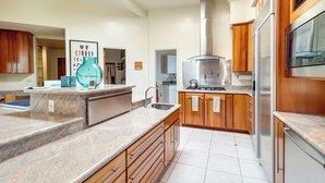 Een moderne keuken met granieten aanrechtbladen, roestvrijstalen apparatuur en houten kastjes.