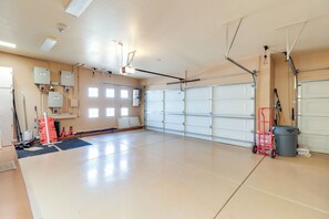 A spacious garage with a large white garage door, overhead lighting, and various tools and equipment.