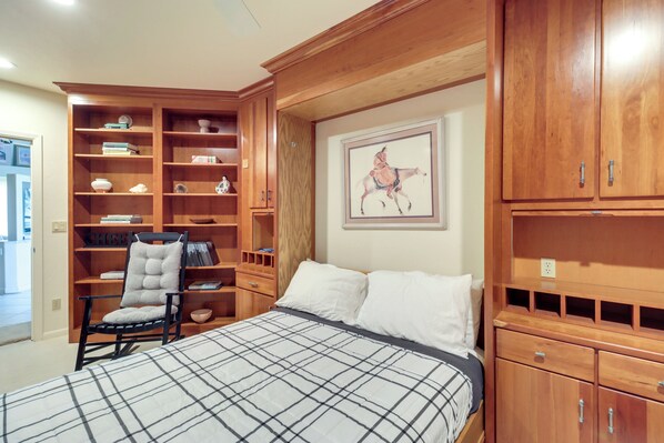 Un dormitorio con cama, una silla, una estantería y un cuadro.