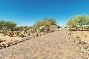 A paved pathway leading to a building with a corrugated metal exterior, surrounded by desert vegetation and trees.