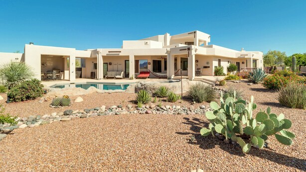Een modern huis met twee verdiepingen, met een zwembad, omgeven door woestijnlandschap met cactussen en agaveplanten.